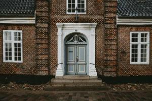 die Vorderansicht eines alten Backsteinhauses mit weißen Fenstern und Eingang mit hellblauen Türen in der ältesten dänischen Stadt Ribe während des regnerischen Herbsttages foto