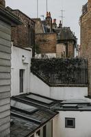 Seitenstraße von Notting Hill in London mit typischen Backsteinmauern und Schornsteinen auf den Dächern von englischen Häusern mit Holzzaun, der mit grünem Busch bedeckt ist und den Hinterhof vom weißen Gebäude trennt foto