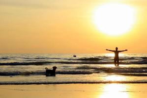 reise nach insel koh chang, thailand. ein mann mit einem hund geht am sonnenuntergangsstrand spazieren. foto