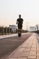 attraktiver europäischer mann fährt an einem sonnigen tag auf einem elektroroller auf einer leeren straße der stadt. foto