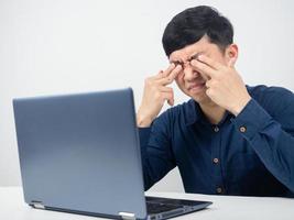 männlicher mitarbeiter mit laptop versucht von der arbeit und fühlt sich überanstrengt, auge zerquetscht foto