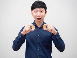 asiatischer mann, der goldenes bitcoin mit erstauntem gesicht auf weißem hintergrund hält foto