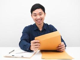 asiatischer mann, der sich glücklich fühlt und lächelt, sitzt an seinem arbeitsplatz und öffnet einen dokumentenumschlag auf dem weißen hintergrund des tisches foto