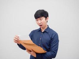 asiatischer mann, der dokumentenumschlag hält und das papier in der hand liest, fühlt sich schockiert auf weißem hintergrund foto