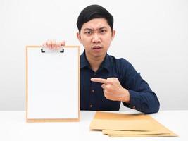 Geschäftsmann zeigt mit dem Finger auf eine leere Dokumententafel in der Hand mit ernsthaften Gesichtsgefühlen auf dem Tisch foto