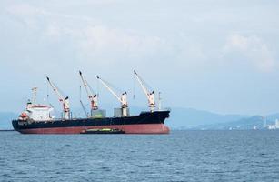 großer kran im industrieschiff im ozean und berg im inselhintergrund, transportschiff in der wirtschaftsseekonzeptlandschaft foto