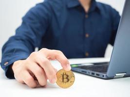 Nahaufnahme der Hand, die goldenes Bitcoin auf dem Tisch mit Laptop-Ernteaufnahme hält foto