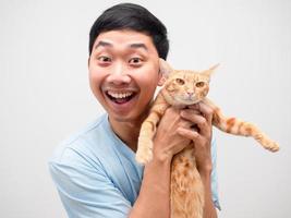 asiatischer mann, der sich glücklich und lustig fühlt, lächeln und eine süße katze in seiner orangefarbenen handfarbe halten foto