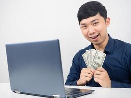 Mann mit glücklichem Gefühl des Laptops, das Geld in der Hand hält foto