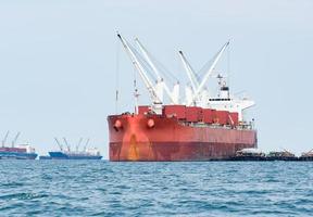 Großes Schiff in roter Farbe mit großem Kran in der Meereslandschaft, Industrieboot im Seelogistikkonzept foto