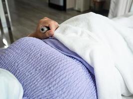 Patient, der im Krankenhaus auf dem Bett liegt und einen medizinischen Schalter in der Hand hält foto