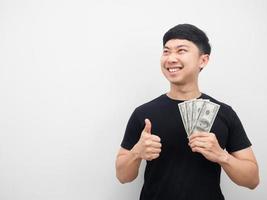 asiatischer mann, der dollargeld und daumen hoch hält, lächelt und kopienraum betrachtet foto
