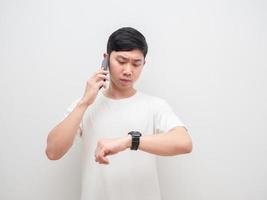 Mann spricht mit Handy und schaut auf seine Uhr ernstes Gesicht auf weißem Hintergrund foto
