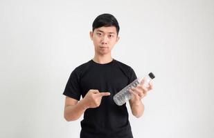 junger asiatischer mann, schwarzes hemd, zeigt finger auf plastikflasche in der hand mit ernstem gesichtsblick in die kamera auf weiß isoliert foto