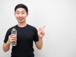 asiatischer mann, schwarzes hemd, das wasserflasche hält, zeigt mit dem finger auf den weißen hintergrund des kopienraums foto