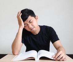 junger mann mit stift ernst und gefühl belastung mit problem berühren seinen kopf von hand mit dem buch auf dem schreibtisch auf weiß isoliert foto