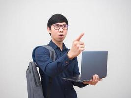 porträt asiatischer mann, der laptop mit rucksack hält, zeigt mit dem finger auf den weißen hintergrund des raumes foto