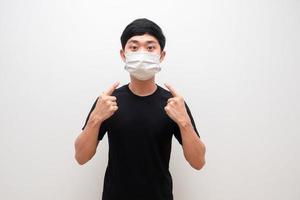 asiatischer mann zeigt mit dem finger auf die schutzmaske auf seinem weißen hintergrund des gesichtsporträts foto