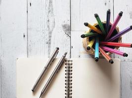 Stift buntes Array Rundschreiben im Karton mit offenem Notizbuch leer mit zwei silbernen Stiften auf weißem Holztisch und Naturlicht der Draufsicht des Sonnenideenkonzepts, Wirtschaft und Bildung foto