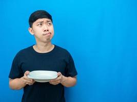 asiatischer mann gestikuliert hungrig, hält teller und schaut auf den kopienraum, der über das abendessen nachdenkt foto