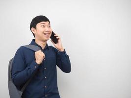 asiatischer mann mit sprechendem handy des rucksacks und lächeln, das kopienraum betrachtet foto