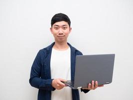 asiatischer mann blaues hemd hält laptop in der hand und schaut in die kamera glückliches gesicht und lächeln auf weiß isoliert foto