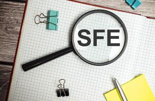 Konzeptbild der Buchhaltungsgeschäftsakronym-SFE-Verkaufskrafteffektivität geschrieben auf weißes Notizbuch mit Lupe foto