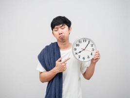 asiatischer mann, der sich schläfrig fühlt, zeigt mit dem finger auf die uhr in der hand, unglückliches gesicht, porträt, weißer hintergrund foto