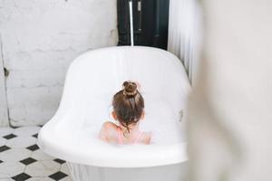 glückliches kleines Mädchen, das sich zu Hause im Bad mit Schaum amüsiert foto