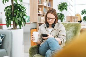 junge Brünette Teenager Mädchen College oder Gymnasiast in Brille mit Handy arbeiten in grüner moderner Bibliothek, öffentlicher Ort, grünes Freiraumbüro foto