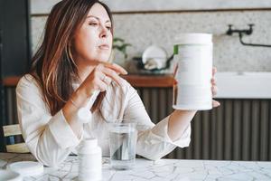 erwachsene lächelnde brünette frau mittleren alters fünfzig jahre beim frühstück mit trockenem instant-protein-vitamin-ergänzungsshake in der küche zu hause foto