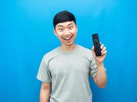 asiatischer mann, der fernbedienungsfernseher hält, glückliches lächeln, blauer hintergrund foto
