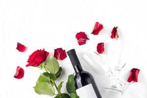 Flasche Wein, Glas und rote Rose mit Blütenblättern auf weißem Hintergrund foto