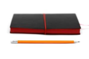 orangefarbener Stift mit rosafarbenem Gummi auf schwarzem Moleskin-Ledernotizbuch isoliert auf Weiß foto