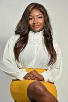 Porträt einer schönen positiven afroamerikanischen Frau in gelbem Rock und weißem Hemd, die im Studio steht und posiert foto