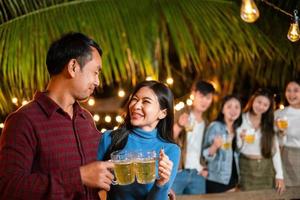 glückliches junges asiatisches paar, das eine party mit freunden hat, während es bier trinkt. foto