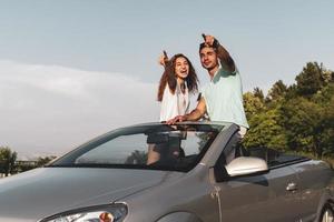 freunde, die spaß bei der autoreise um die welt haben. Verliebtes Paar mit erhobenen Armen auf einem Cabrio. foto