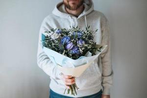 Junger bärtiger Mann in grauem Hoodie mit Blumenstrauß in den Händen auf grauem Hintergrund foto