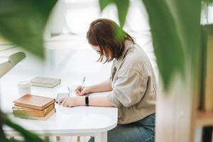 Junges Teenager-Mädchen mit Brille, das Hausaufgaben mit dem Handy am öffentlichen Ort der modernen Bibliothek macht, grünes Freiraumbüro. Universitäts- oder College-Student hören Online-Kurs in der Bildungsklasse foto