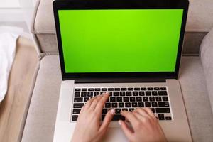 junge Frau mit Computer mit Mock-up Chrome Key Green Computermonitor. Fernunterricht Online-Bildung und Arbeit. Mädchen arbeiten im Büro von zu Hause aus auf der freiberuflichen Couch. schreiben, tippen. foto