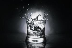 Eiswürfel, der in ein mit Wasser gefülltes Glas spritzt foto