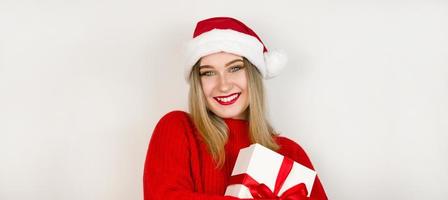 weihnachtsfahne mit platz für text mit hübschem mädchen in weihnachtsmütze und rotem pullover, der geschenk gegen weißen hintergrund hält foto