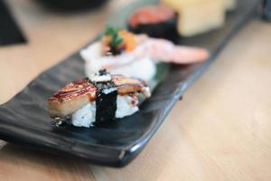Selektiver Fokus auf Gänseleber-Sushi mit einer Unschärfe von anderem Sushi auf der rechteckigen schwarzen Keramikplatte.