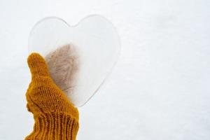 Herzen - ein Symbol der Liebe, aus Eis, werden von einer Hand in warmen gelben Strickfäustlingen gehalten. Valentinstag. romantisches Konzept. Platz kopieren. foto