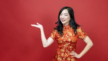 asiatische frau mit rotem cheongsam oder qipao, die auf geschenk für den feiertag des chinesischen neujahrsfests zeigt, isoliert auf rotem hintergrundkonzept foto