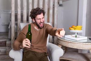 Aufgeregter Sportfan sitzt auf einem Sofa und sieht sich ein Spiel im Fernsehen an. freizeit-, sport-, unterhaltungs- und menschenkonzept - mann, der zu hause fußball oder fußballspiel im fernsehen sieht und bier trinkt foto