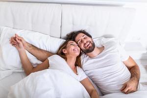 junges Liebespaar im Bett. junges Paar, das im Bett liegt und lacht, während es sich gegenseitig kitzelt. glückliches sinnliches junges paar, das morgens zusammen im bett liegt foto