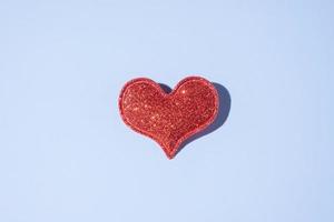 rote Glitzerherzform auf blauem Hintergrund mit hartem Schatten. Valentinstag minimalistisches Symbol Liebe foto