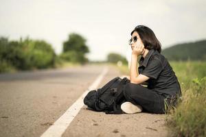 Frau sitzt mit Rucksack per Anhalter auf einer Straße in der Landschaft foto