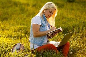 zufriedene Frau beim Sitzen und Lesen von Büchern im Park foto